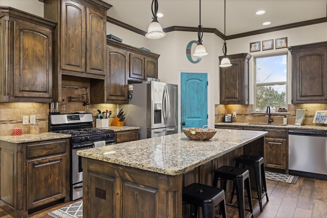 kitchen with appliances with stainless steel finishes, decorative backsplash, hanging light fixtures, a kitchen island, and dark brown cabinetry