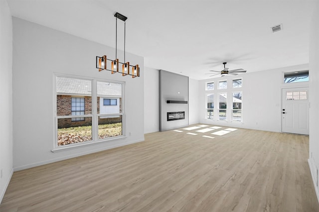 unfurnished living room featuring light wood-type flooring and ceiling fan with notable chandelier