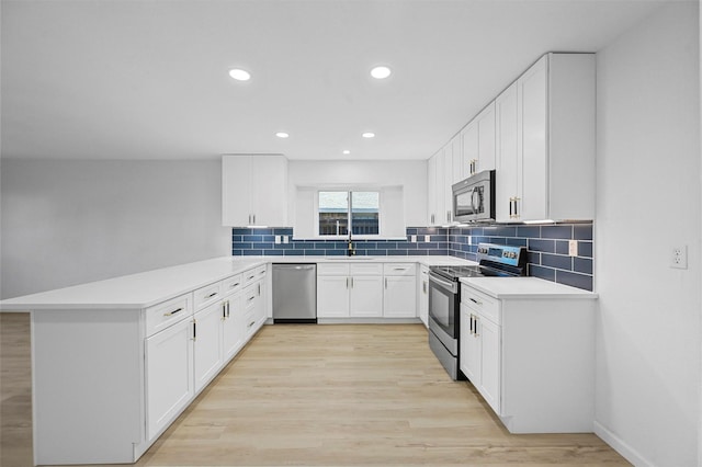 kitchen with appliances with stainless steel finishes, decorative backsplash, white cabinets, sink, and kitchen peninsula