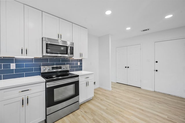 kitchen featuring backsplash, light wood-type flooring, white cabinets, and appliances with stainless steel finishes