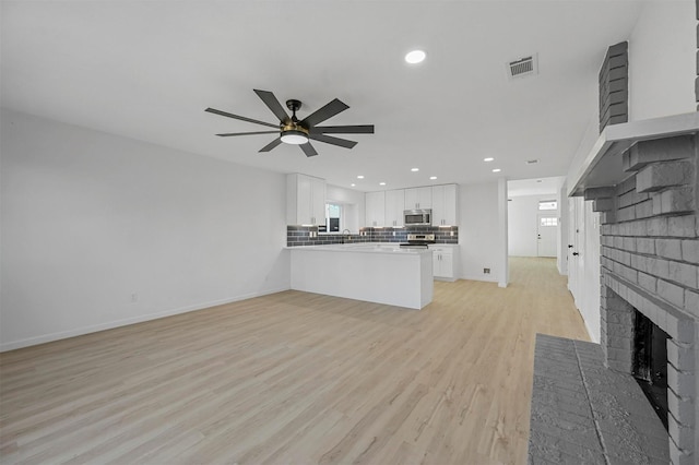 unfurnished living room with sink, ceiling fan, a brick fireplace, and light hardwood / wood-style flooring