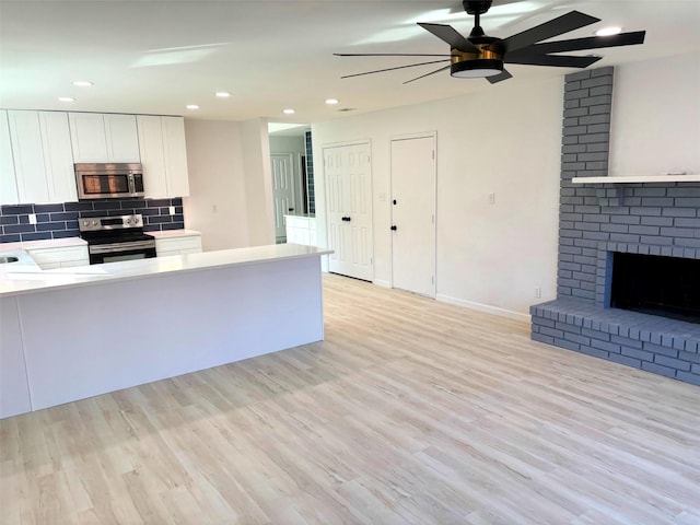 kitchen with tasteful backsplash, a brick fireplace, light hardwood / wood-style flooring, stainless steel appliances, and white cabinets