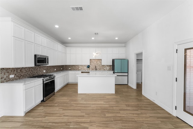 kitchen featuring stainless steel appliances, tasteful backsplash, white cabinets, a kitchen island, and decorative light fixtures