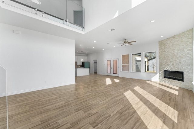 unfurnished living room with a high ceiling, a fireplace, ceiling fan, and light wood-type flooring