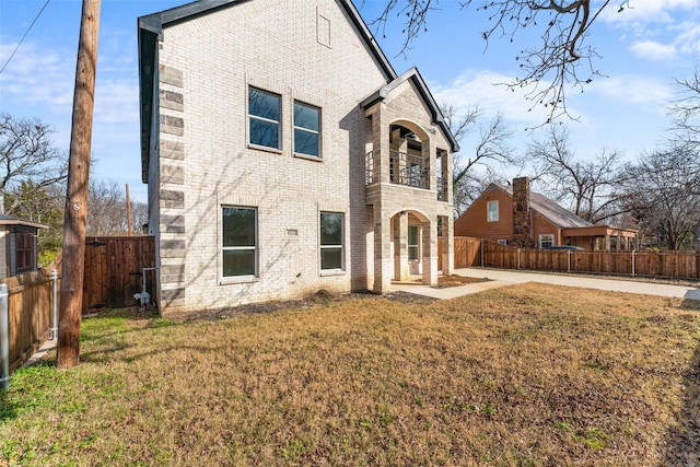 view of front of home with brick siding, a front lawn, a fenced backyard, and a balcony