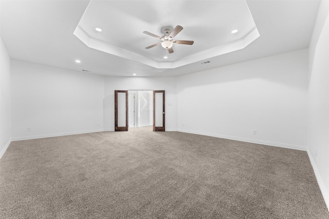 empty room with a raised ceiling, ceiling fan, and carpet flooring