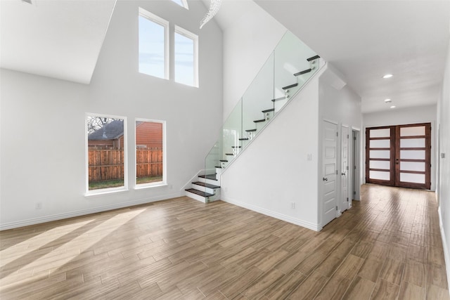 unfurnished living room featuring a towering ceiling, light wood-type flooring, and french doors