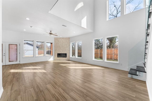 unfurnished living room with ceiling fan, a towering ceiling, a fireplace, and light hardwood / wood-style floors