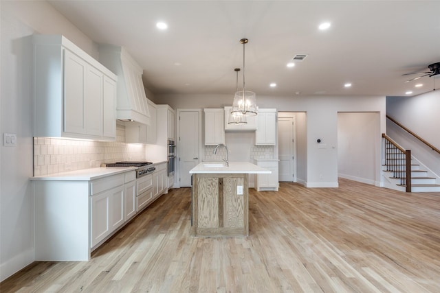 kitchen with decorative light fixtures, light hardwood / wood-style flooring, white cabinets, and a kitchen island with sink