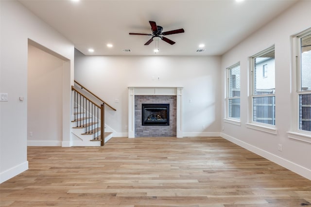 unfurnished living room featuring ceiling fan, a brick fireplace, and light hardwood / wood-style flooring