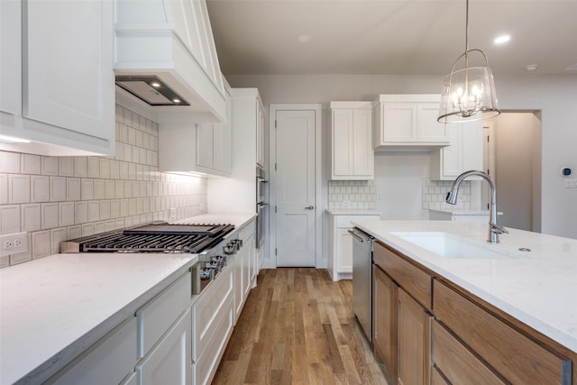 kitchen with premium range hood, stainless steel appliances, white cabinets, light stone counters, and sink