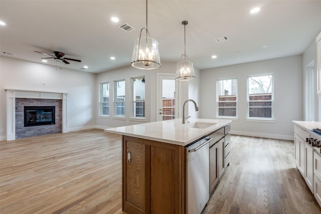 kitchen featuring decorative light fixtures, stainless steel dishwasher, sink, white cabinetry, and an island with sink