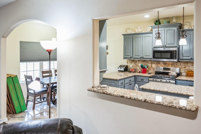 kitchen with decorative light fixtures, backsplash, kitchen peninsula, light stone countertops, and appliances with stainless steel finishes