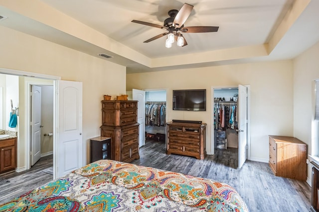 bedroom featuring a spacious closet, a tray ceiling, a closet, ceiling fan, and ensuite bathroom