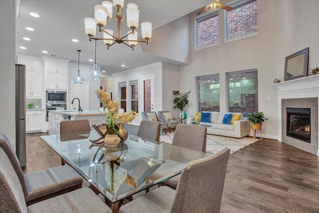 dining room with a tiled fireplace, wood-type flooring, ornamental molding, ceiling fan with notable chandelier, and sink