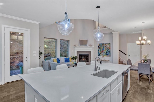 kitchen with white cabinets, sink, hanging light fixtures, stainless steel dishwasher, and a tiled fireplace