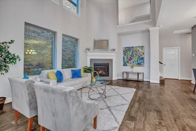 living room with a tiled fireplace, a towering ceiling, and dark hardwood / wood-style flooring