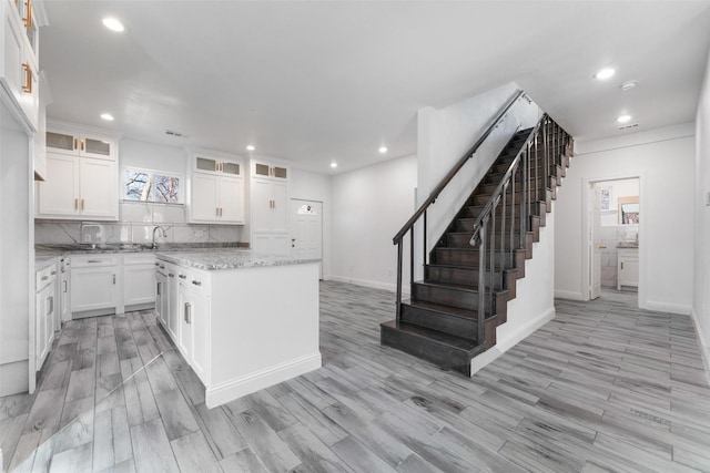 kitchen featuring white cabinetry, a kitchen island, light stone counters, and light hardwood / wood-style flooring