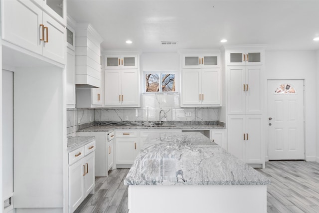 kitchen with sink, light stone countertops, a center island, and white cabinets