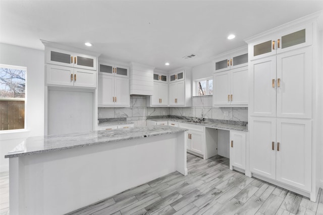 kitchen with decorative backsplash, light stone countertops, a center island, and white cabinets