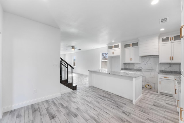 kitchen with light hardwood / wood-style flooring, white cabinetry, backsplash, light stone countertops, and a kitchen island