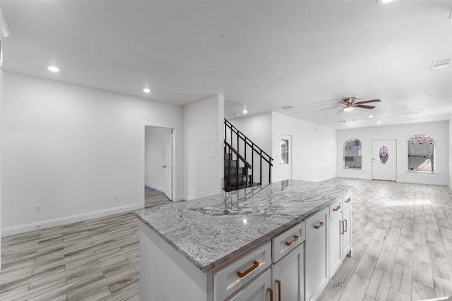 kitchen with white cabinets, a center island, ceiling fan, light stone counters, and light wood-type flooring