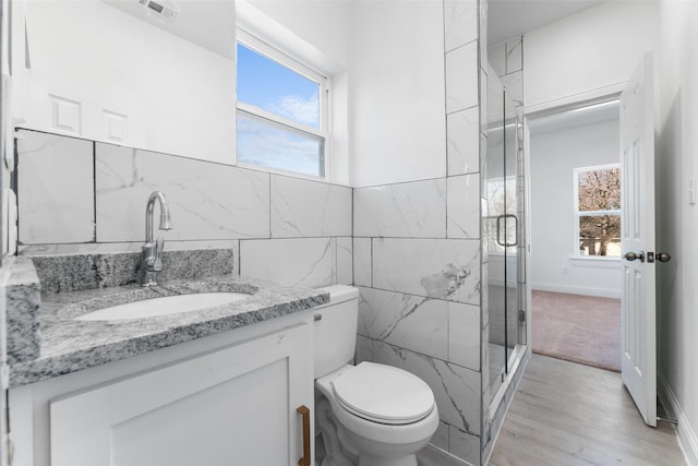 bathroom featuring toilet, wood-type flooring, tile walls, vanity, and a shower with door