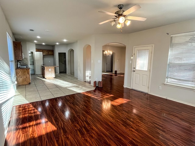 unfurnished living room with ceiling fan with notable chandelier, sink, and light wood-type flooring