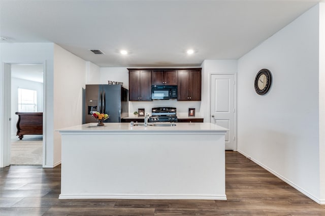 kitchen featuring dark brown cabinetry, stainless steel fridge, an island with sink, and range