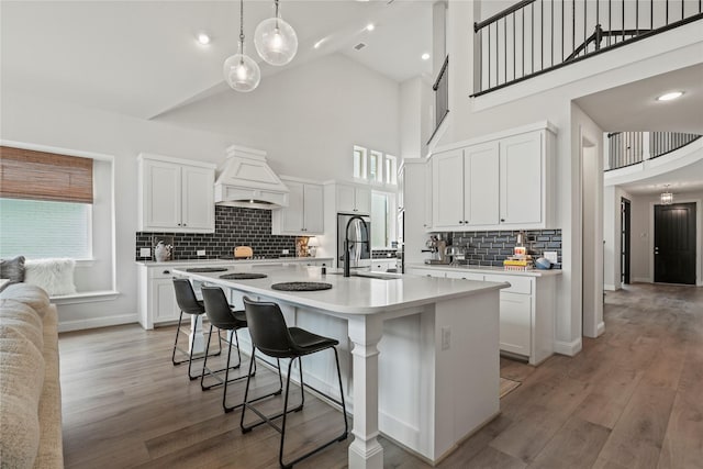 kitchen with white cabinets, a kitchen island with sink, a high ceiling, and custom range hood