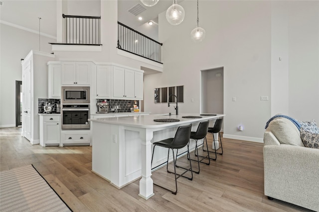 kitchen featuring a high ceiling, white cabinets, a center island with sink, and stainless steel appliances