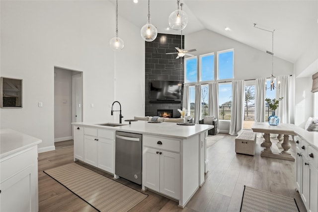 kitchen featuring a center island with sink, stainless steel dishwasher, a large fireplace, sink, and white cabinetry