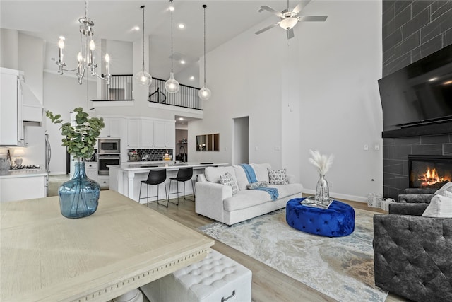 living room with ceiling fan with notable chandelier, light hardwood / wood-style floors, a fireplace, and high vaulted ceiling