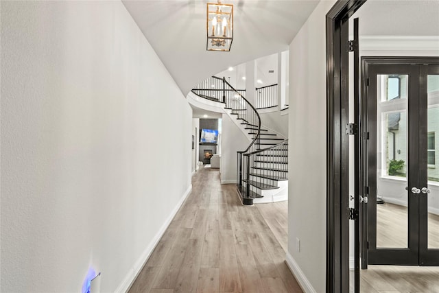 entryway with french doors, a notable chandelier, crown molding, and light hardwood / wood-style floors