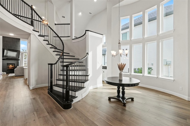 staircase with hardwood / wood-style flooring, an inviting chandelier, a large fireplace, and a high ceiling