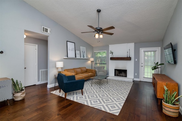 living room with ceiling fan, vaulted ceiling, dark hardwood / wood-style flooring, a fireplace, and a textured ceiling