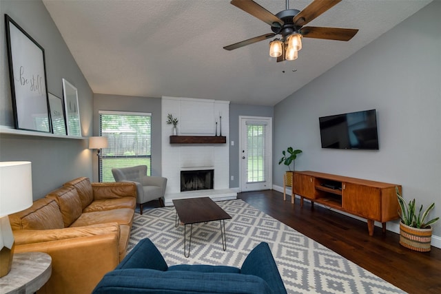 living room featuring ceiling fan, a large fireplace, a textured ceiling, dark hardwood / wood-style flooring, and vaulted ceiling