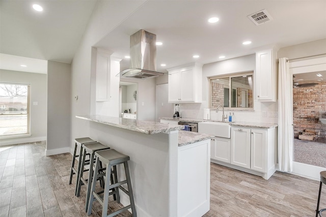 kitchen featuring island range hood, white cabinets, light stone counters, and sink