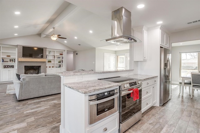 kitchen featuring light stone countertops, white cabinets, appliances with stainless steel finishes, island range hood, and a brick fireplace