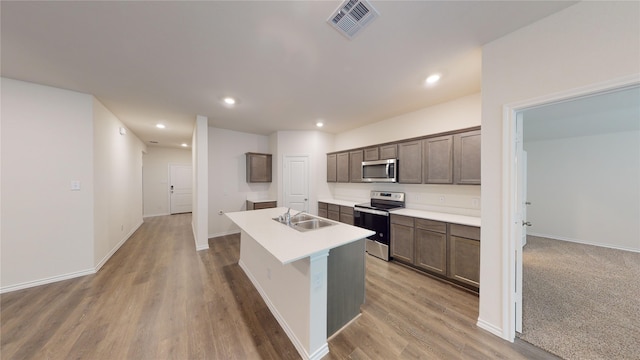 kitchen featuring hardwood / wood-style floors, dark brown cabinetry, stainless steel appliances, sink, and a center island with sink