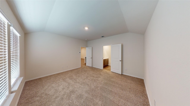 unfurnished bedroom featuring multiple windows, ensuite bathroom, light carpet, and vaulted ceiling