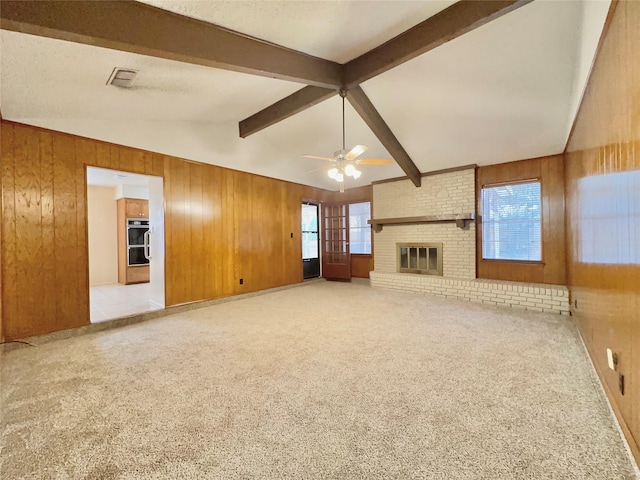 unfurnished living room with wooden walls, ceiling fan, a fireplace, light colored carpet, and lofted ceiling with beams