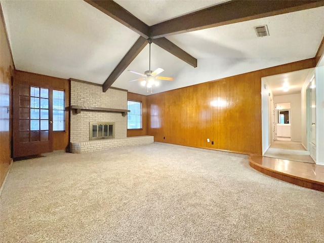 unfurnished living room featuring wooden walls, ceiling fan, a fireplace, light colored carpet, and lofted ceiling with beams