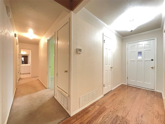 entryway with a textured ceiling, light carpet, and ornamental molding