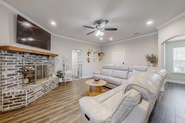 living room featuring ceiling fan, dark hardwood / wood-style flooring, crown molding, and a fireplace