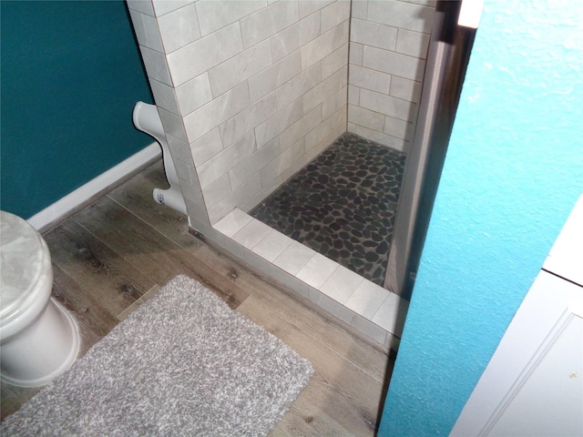 bathroom featuring toilet, a tile shower, and hardwood / wood-style flooring