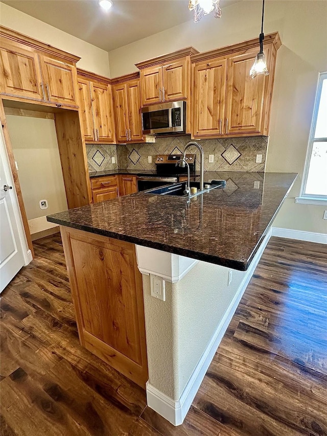 kitchen with dark hardwood / wood-style floors, pendant lighting, kitchen peninsula, sink, and dark stone counters