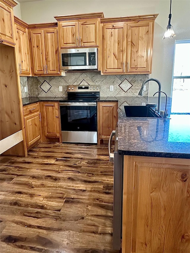 kitchen with dark stone countertops, sink, hanging light fixtures, appliances with stainless steel finishes, and dark wood-type flooring