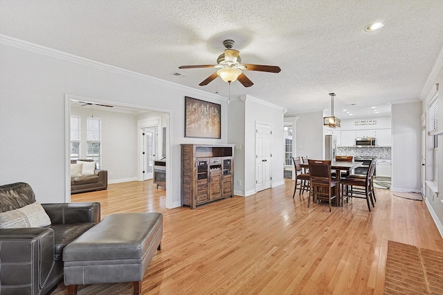 living room featuring crown molding, light hardwood / wood-style flooring, a textured ceiling, and ceiling fan