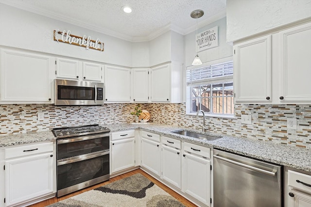 kitchen with appliances with stainless steel finishes, decorative light fixtures, sink, white cabinets, and crown molding